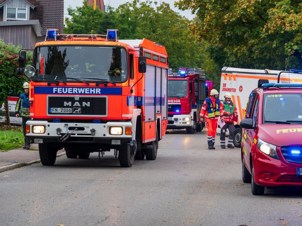Mehrere Fahrzeuge von Feuerwehr und Johannitern stehen mit Blaulicht in zwei Reihen auf einer Straße.
