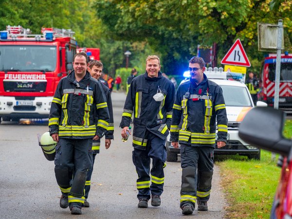 Vier Feuerwehrmänner der Feuerwehr Langenargen laufen nach getaner Arbeit entlang einer Straße. Im Hintergrund mehrere Einsatzfahrzeuge.
