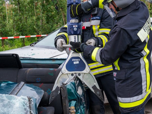 Zwei Feuerwehrmänner bringen einen Akkuspreizer an einem Unfallfahrzeug zum Einsatz.